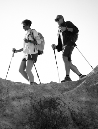 Two people wearing Apple Watch devices and hiking on a rocky trail with poles and gear